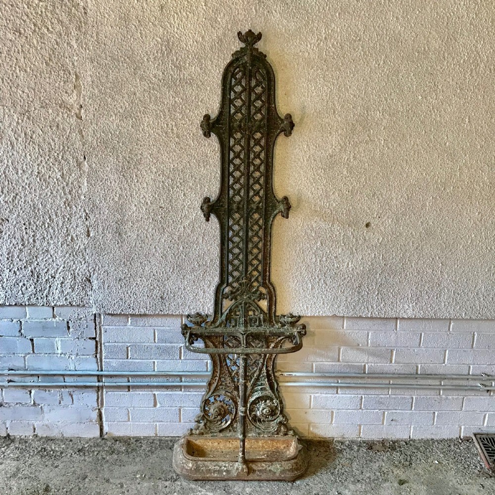 A tall Victorian cast iron hall stand featuring a lattice backrest, multiple coat hooks, scroll motifs, and an integrated drip tray at the base.