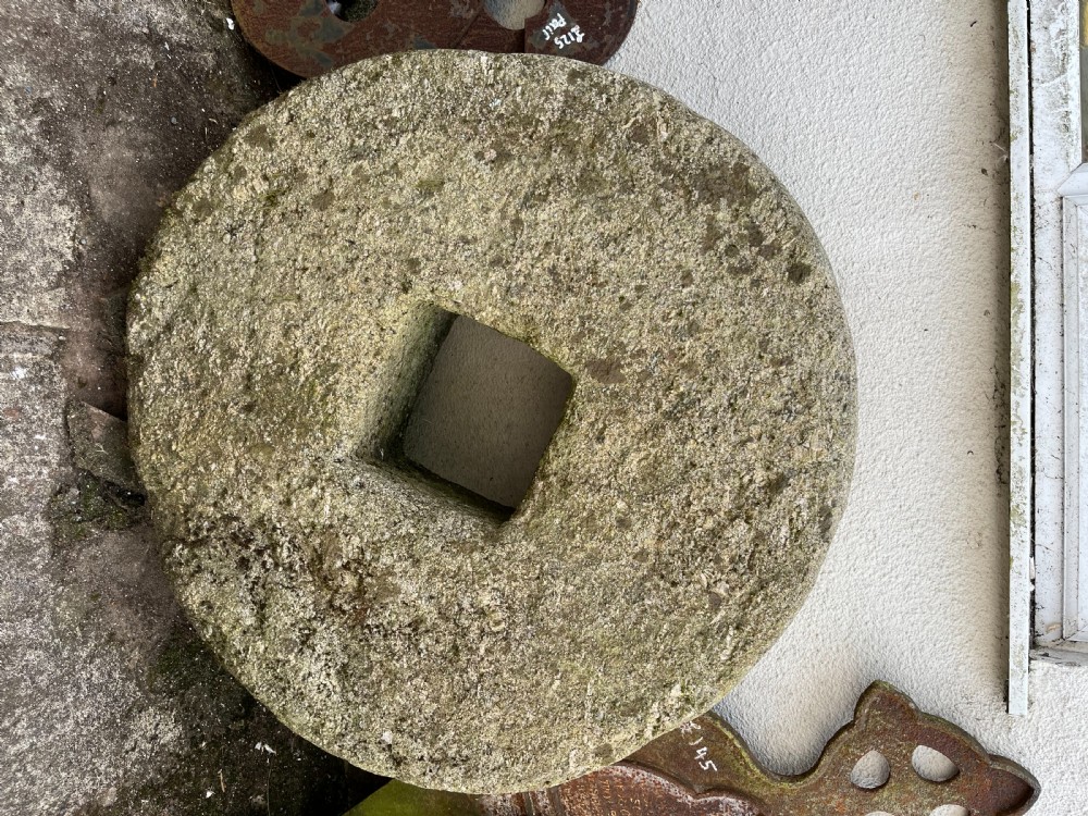 A circular 19th-century grey granite grindstone featuring a hand-chiselled textured surface and a square central aperture.