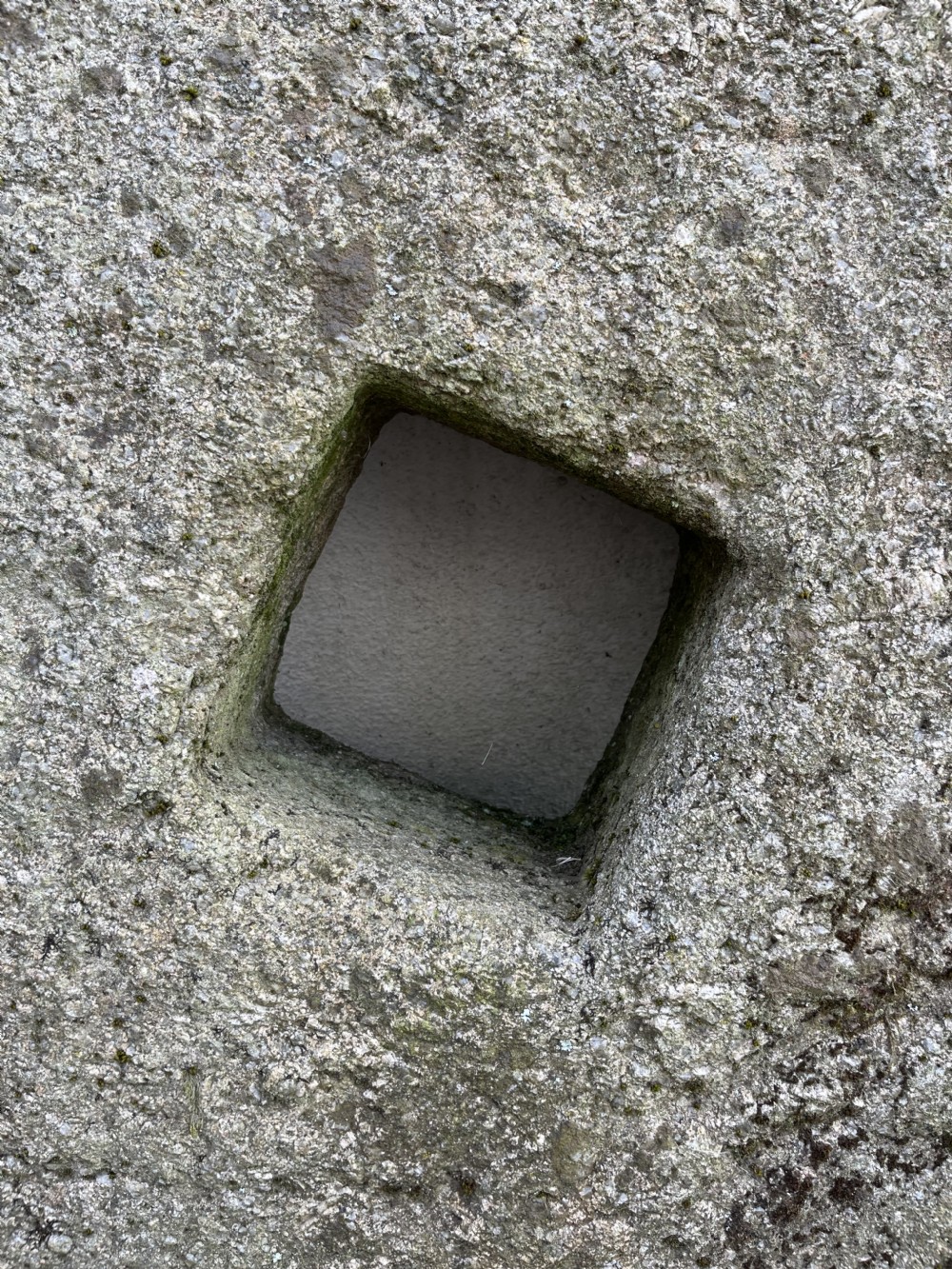 A circular 19th-century grey granite grindstone featuring a hand-chiselled textured surface and a square central aperture. View II