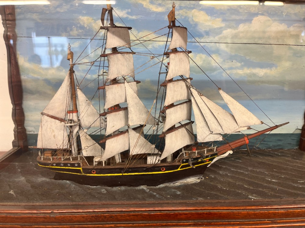A 19th-century English ship diorama featuring a detailed three-masted sailing vessel set against a painted ocean background inside a glazed wooden case with turned corner posts. View II