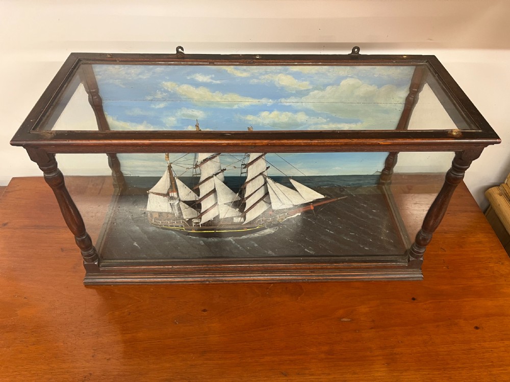 A 19th-century English ship diorama featuring a detailed three-masted sailing vessel set against a painted ocean background inside a glazed wooden case with turned corner posts. View V