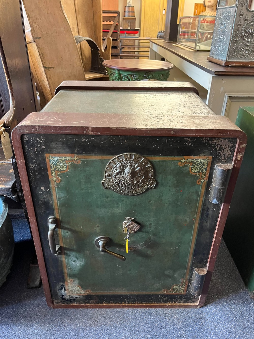 A heavy turn-of-the-century Milners iron safe featuring dark green painted panels, a brass crest emblem, and decorative corner detailing.