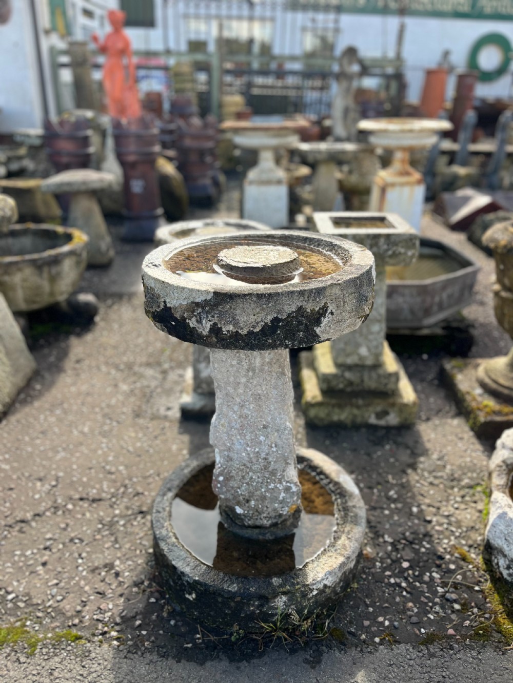 A 19th-century carved Purbeck stone bird bath featuring a weathered cylindrical column pedestal set within a lower basin and supporting a circular upper water basin with natural lichen patination.