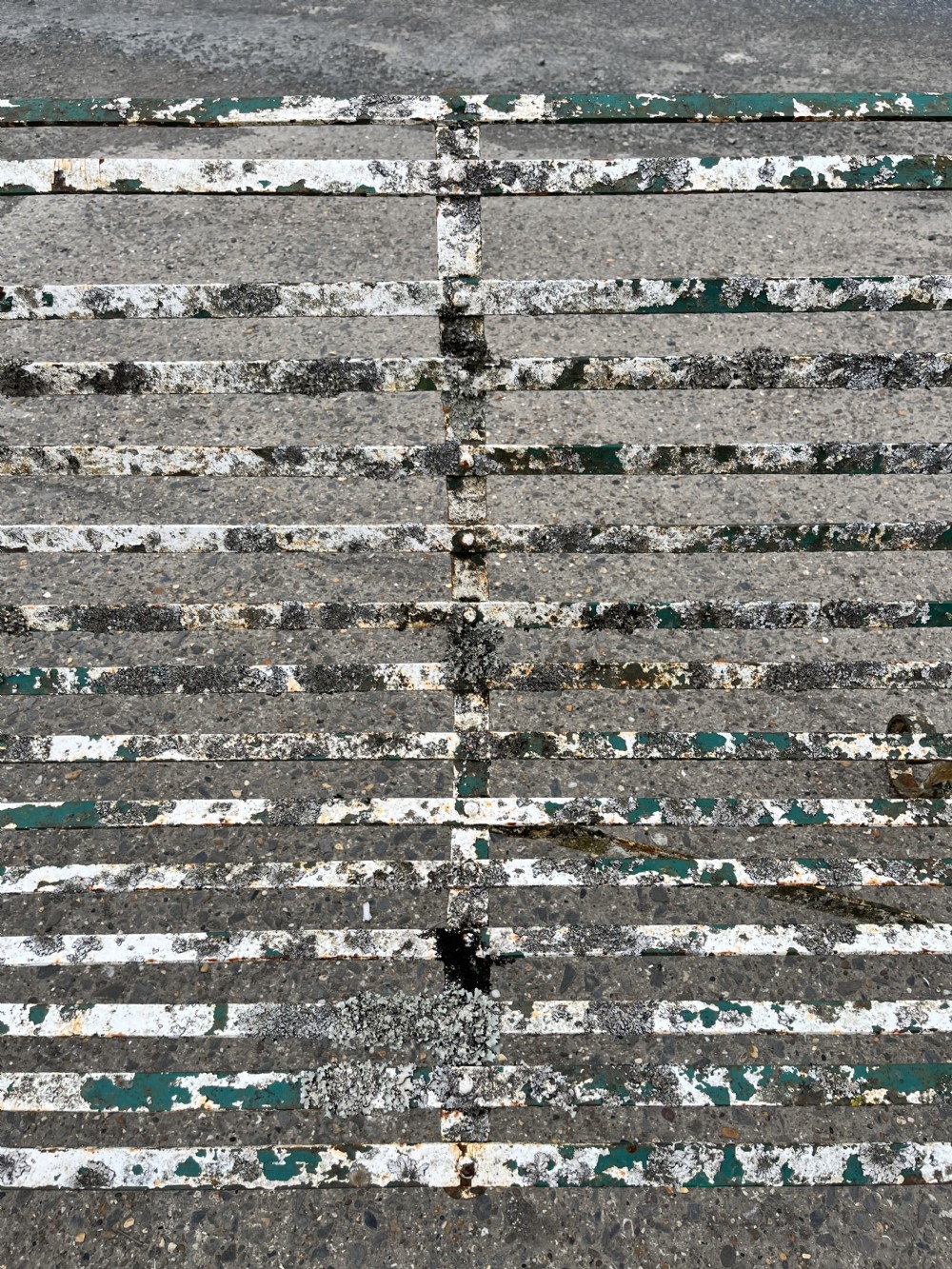 A Victorian wrought iron garden bench featuring horizontal metal strapwork, curved scroll armrests, and a distressed green and white painted finish. View VII
