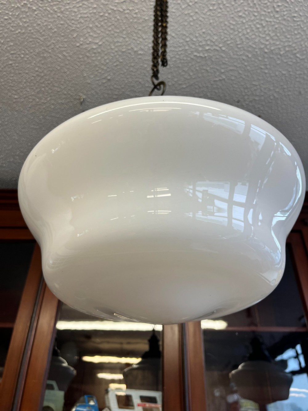 An early 20th-century white opaline glass chapel pendant light featuring a wide rounded shade, an aged brass gallery, and a suspension chain. View V