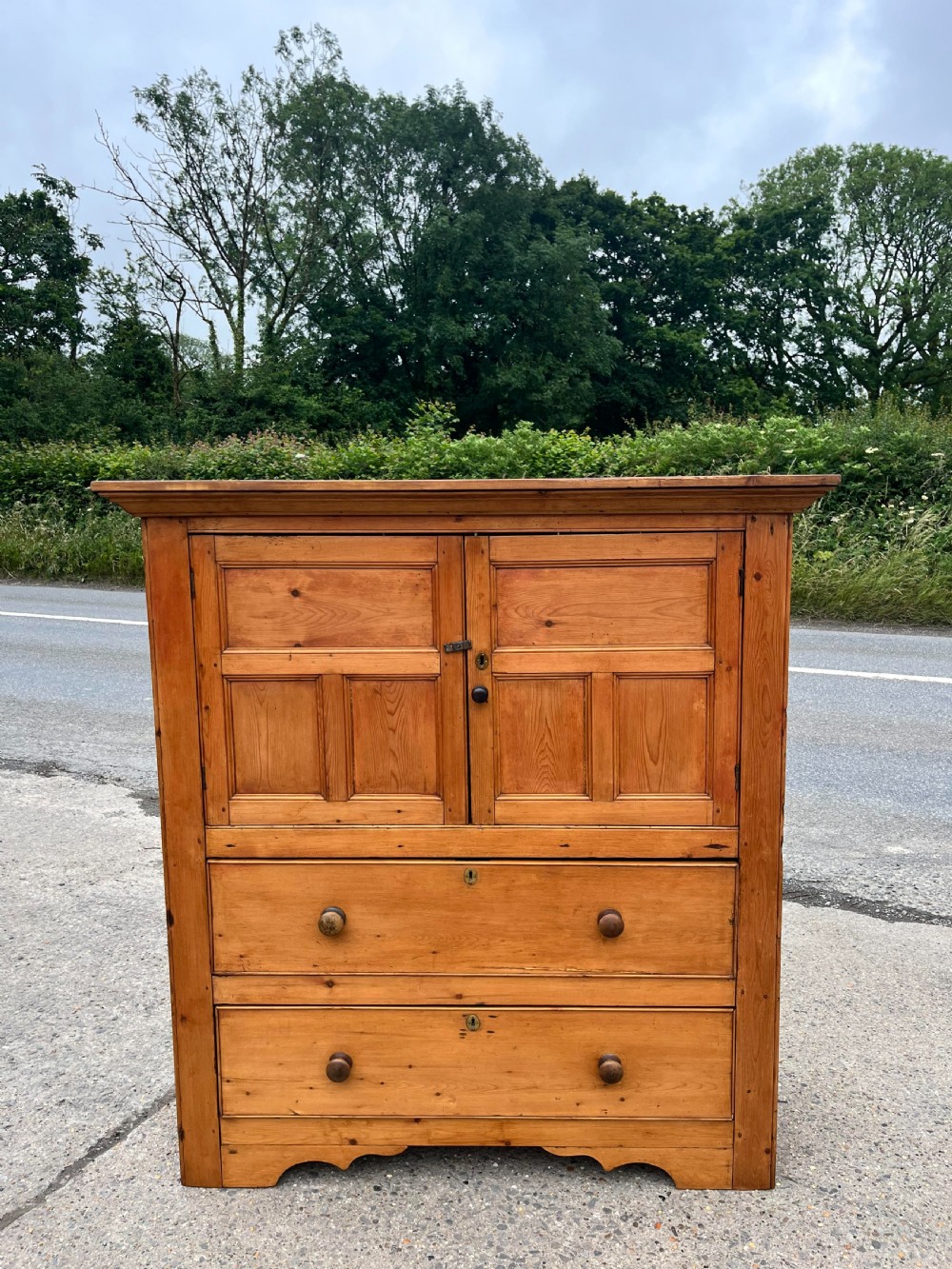 An early 19th-century Georgian pine linen cupboard featuring two upper panelled doors over two wide drawers with wooden turned knobs.