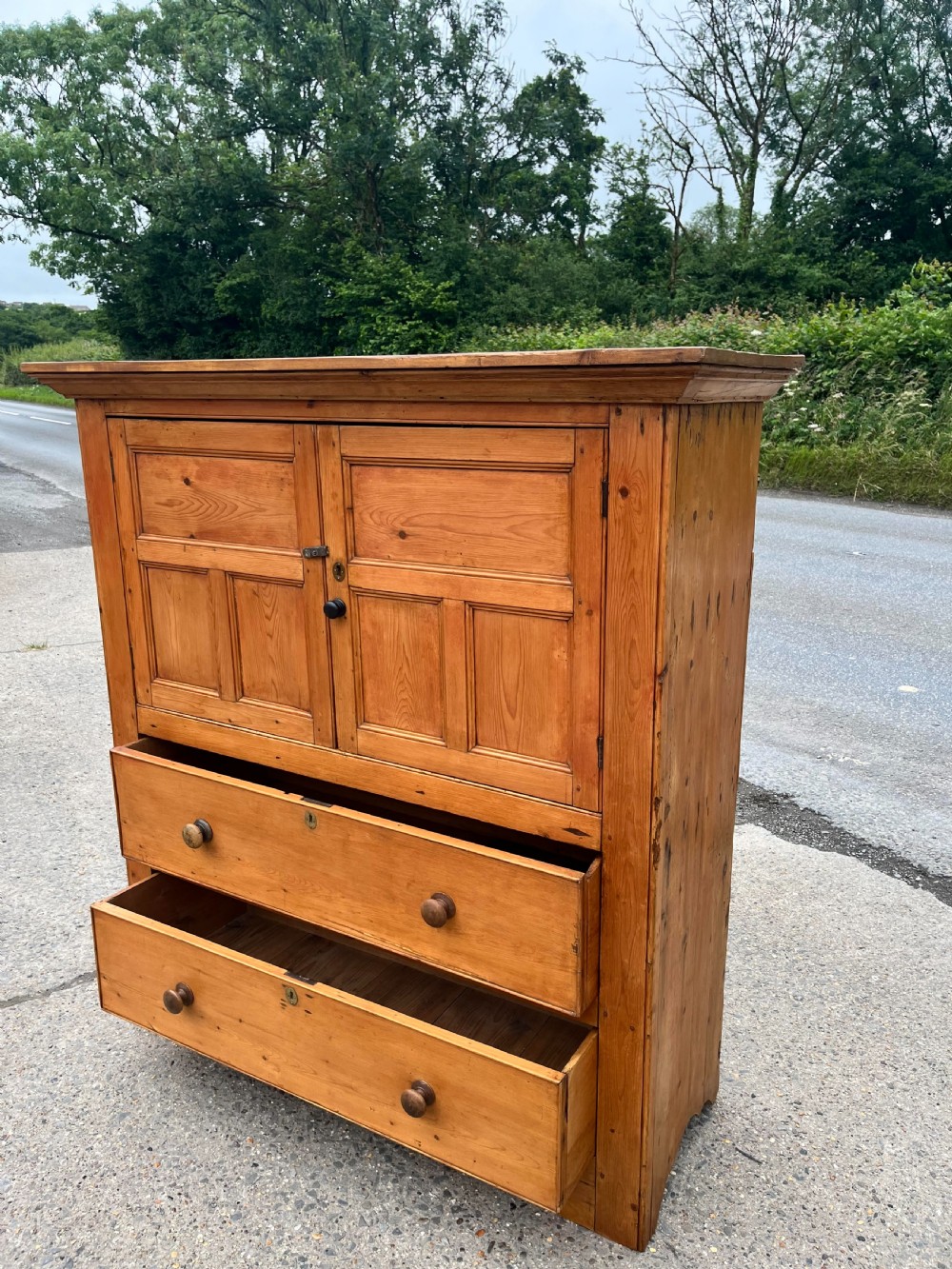 An early 19th-century Georgian pine linen cupboard featuring two upper panelled doors over two wide drawers with wooden turned knobs. View II