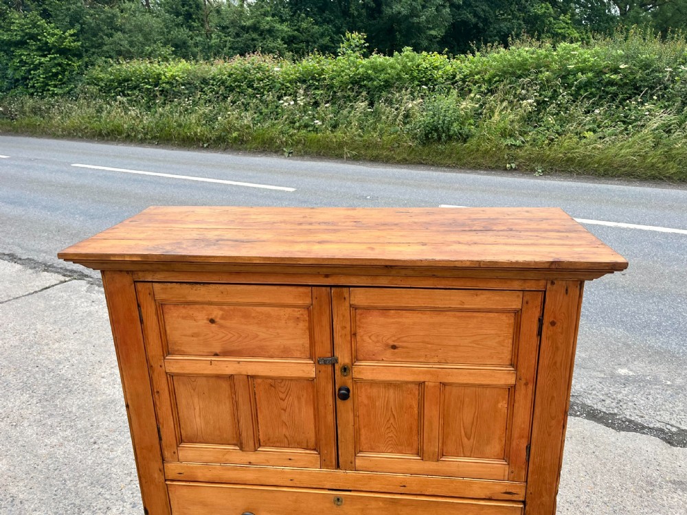 An early 19th-century Georgian pine linen cupboard featuring two upper panelled doors over two wide drawers with wooden turned knobs. View V
