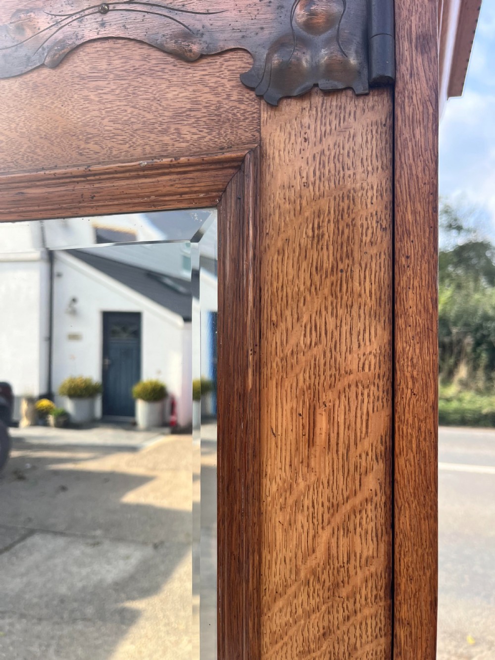 A turn-of-the-century Edwardian oak gentlemans wardrobe featuring a full-length mirrored door, relief-carved central panel, three carved front drawers, and iron strap hinges. View V