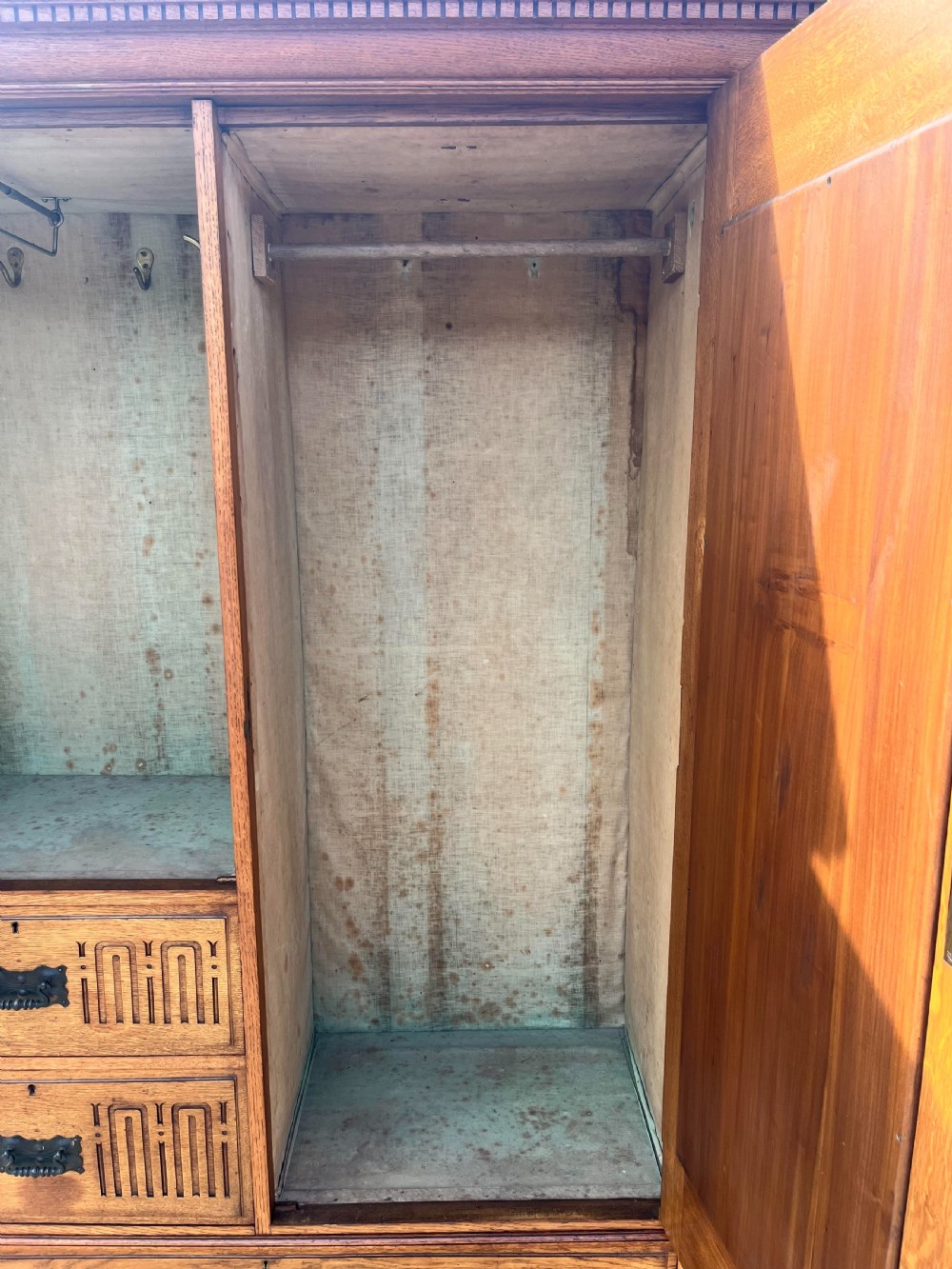 A turn-of-the-century Edwardian oak gentlemans wardrobe featuring a full-length mirrored door, relief-carved central panel, three carved front drawers, and iron strap hinges. View VI