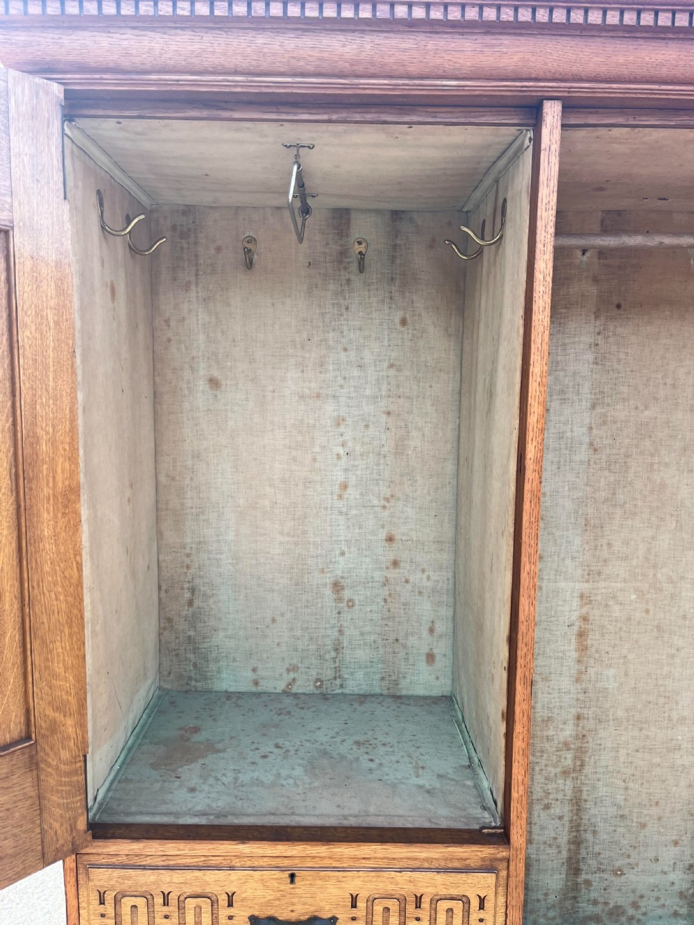 A turn-of-the-century Edwardian oak gentlemans wardrobe featuring a full-length mirrored door, relief-carved central panel, three carved front drawers, and iron strap hinges. View VII