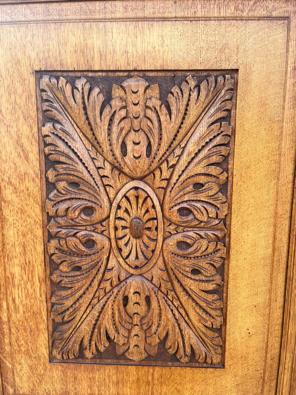 A turn-of-the-century Edwardian oak gentlemans wardrobe featuring a full-length mirrored door, relief-carved central panel, three carved front drawers, and iron strap hinges. View VIII