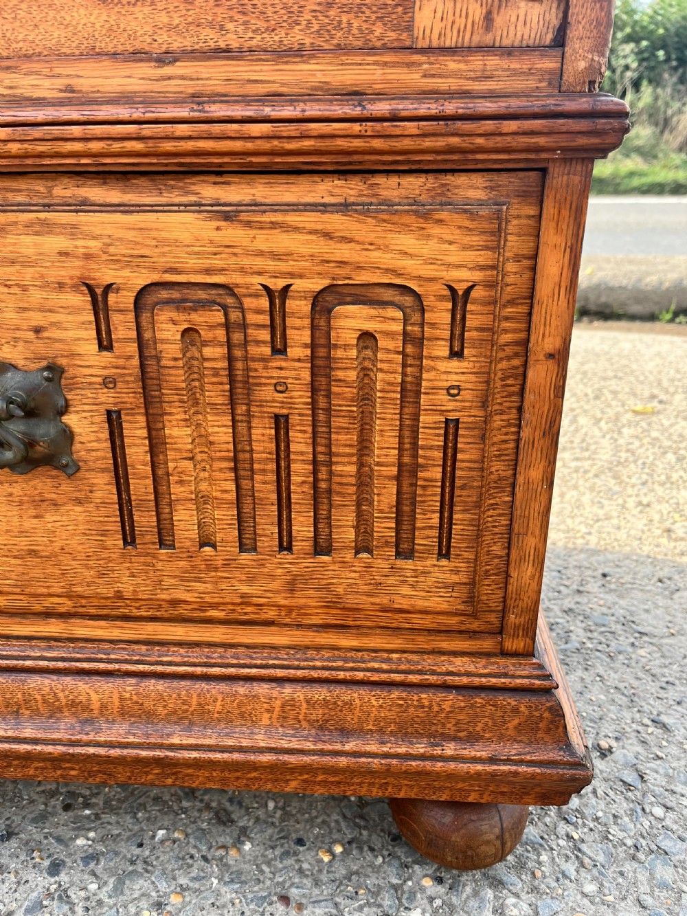 A turn-of-the-century Edwardian oak gentlemans wardrobe featuring a full-length mirrored door, relief-carved central panel, three carved front drawers, and iron strap hinges. View XV