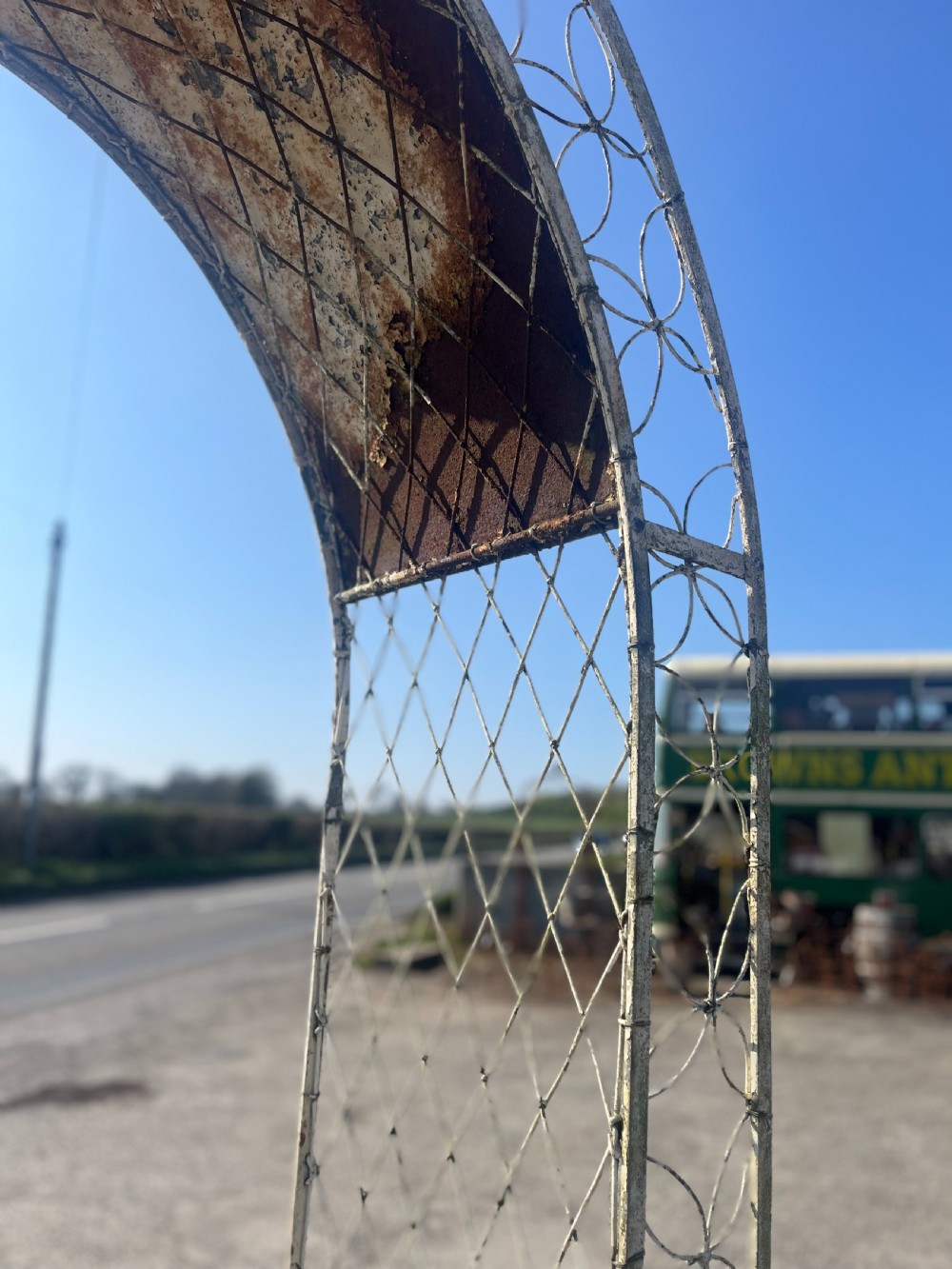 A tall early 20th-century wrought iron garden arch featuring interlocking circular side panels, a wirework canopy, and a weathered cream painted finish. View V