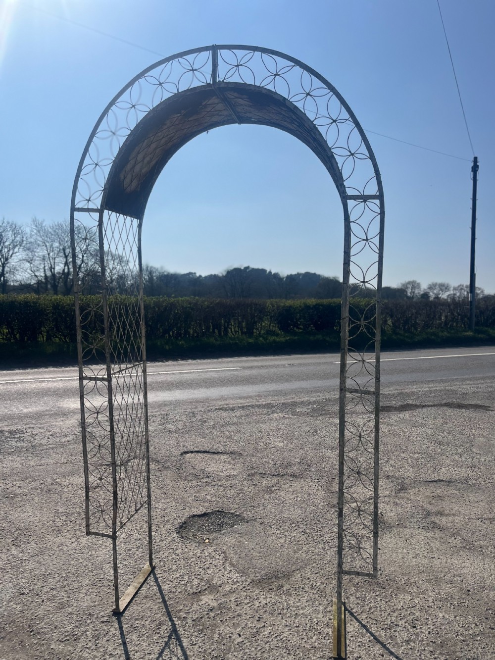 A tall early 20th-century wrought iron garden arch featuring interlocking circular side panels, a wirework canopy, and a weathered cream painted finish.