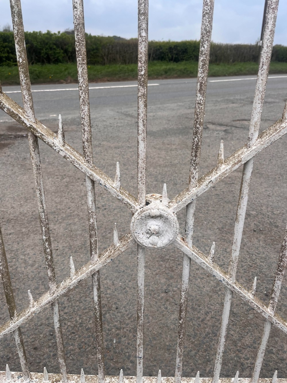A mid-19th-century wrought iron estate gate with white paint, vertical railings, spearhead finials, and central diamond cross-bracing with rosettes. View V
