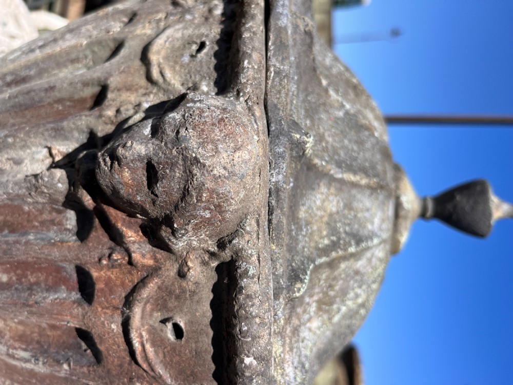 A 19th-century weathered lead garden urn featuring a pointed lid, cherub head relief, swags, and a fluted body on a circular base. View V