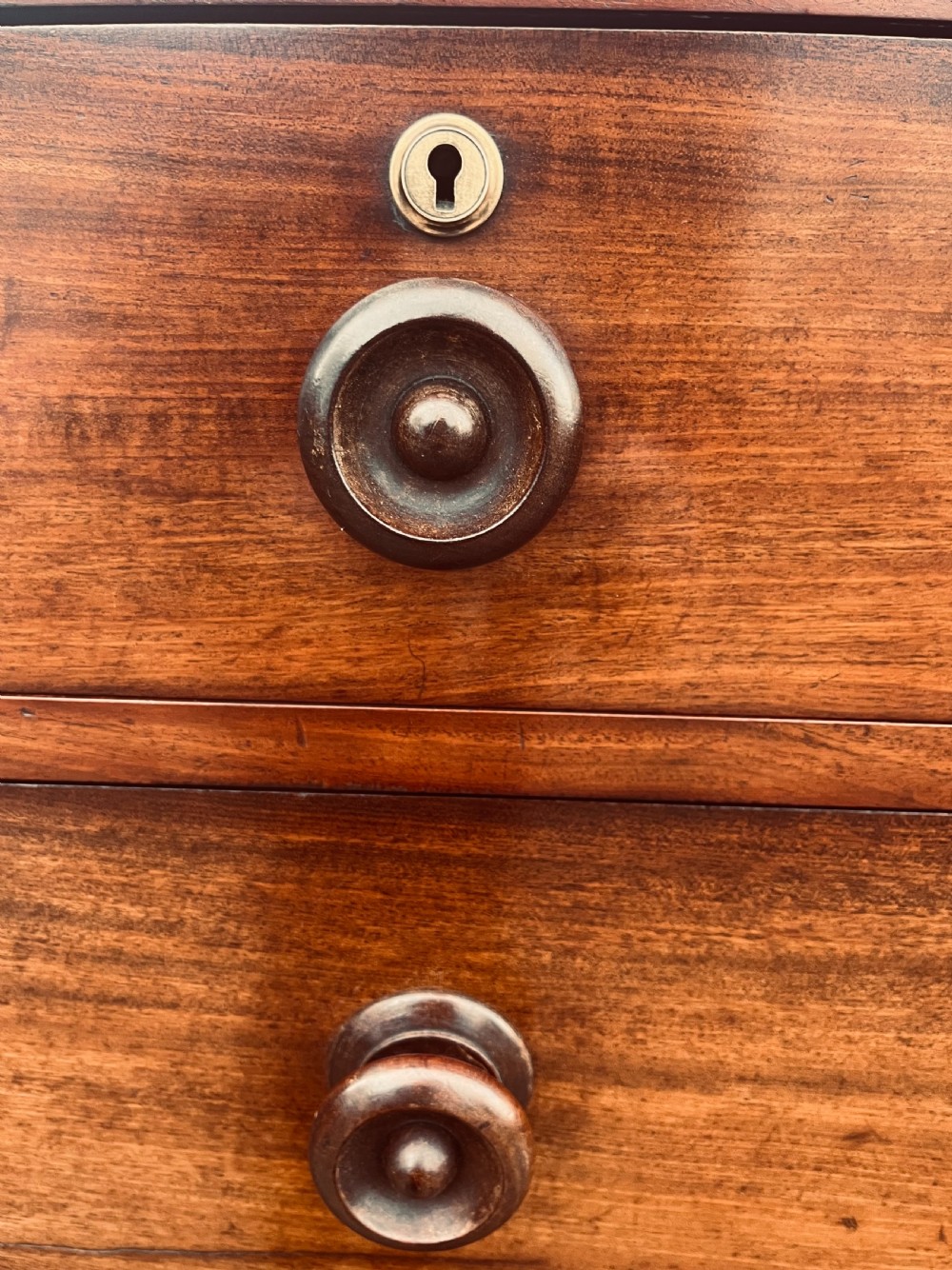A late Georgian mahogany chest of drawers featuring two short drawers over four long graduated drawers with turned handles and brass keyhole escutcheons. View VII