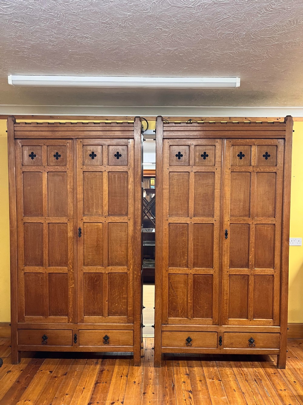 A pair of tall Victorian ecclesiastical oak cupboards featuring panelled double doors, lower drawers, and quatrefoil cut-outs.
