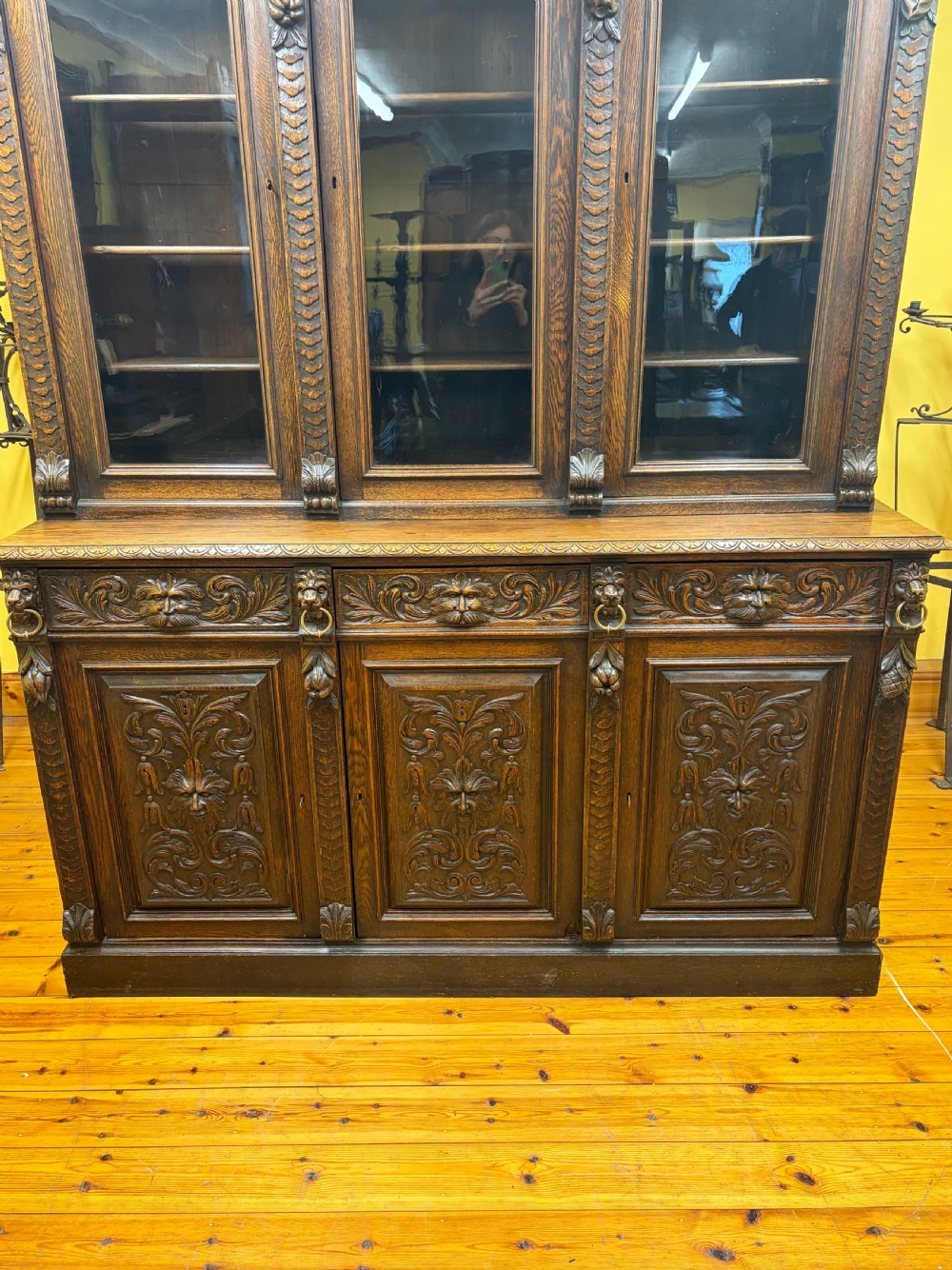 A large Victorian dark oak bookcase featuring three glass upper doors, three carved drawers, three carved lower cabinet doors, and a decorative scroll pediment. View XV