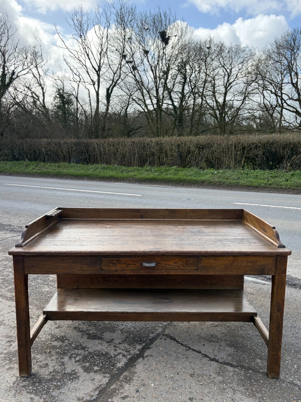 A 1920s solid oak post office sorting table featuring a raised top gallery, single drawer, and an open lower shelf.