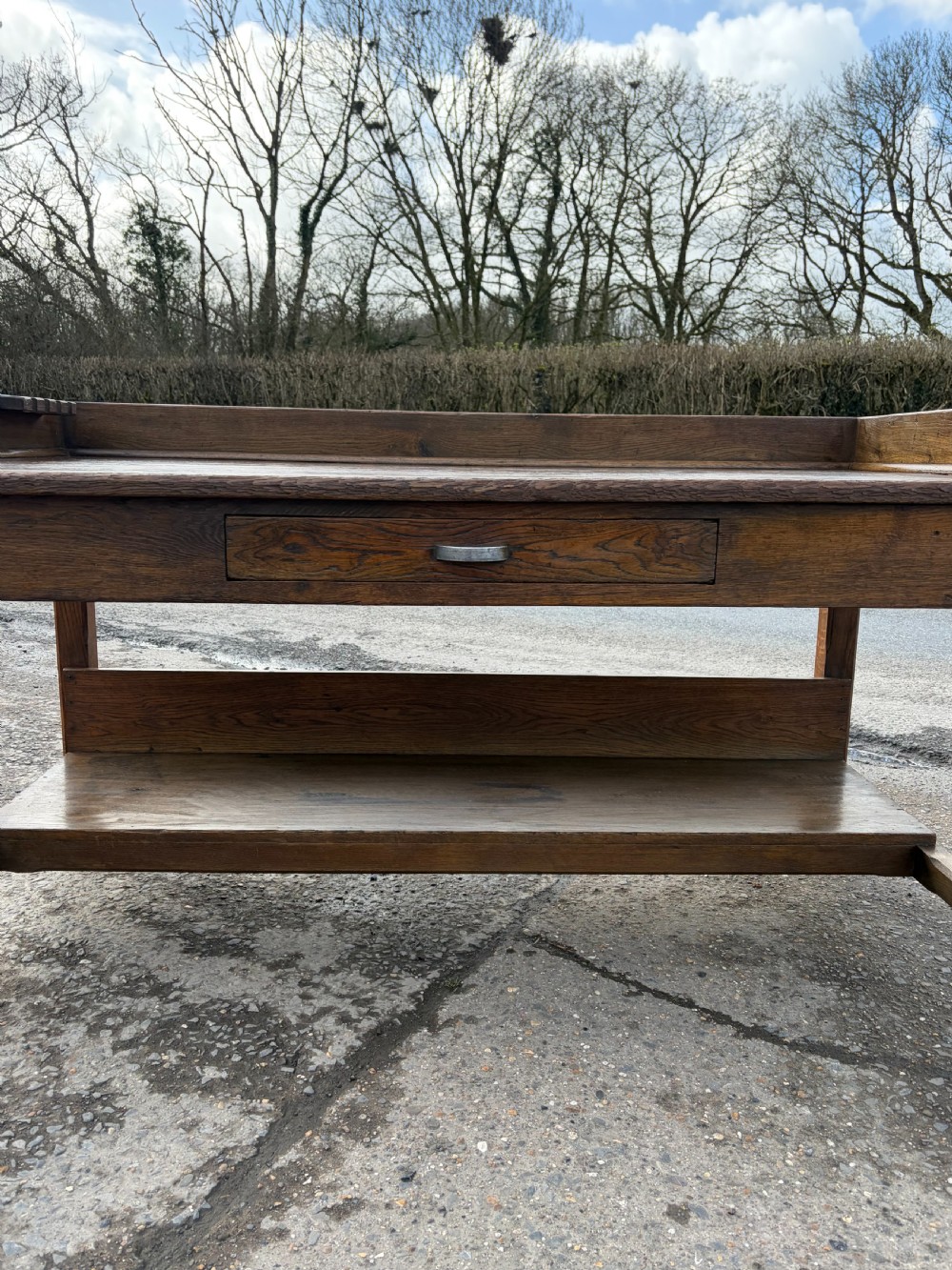 A 1920s solid oak post office sorting table featuring a raised top gallery, single drawer, and an open lower shelf. View V