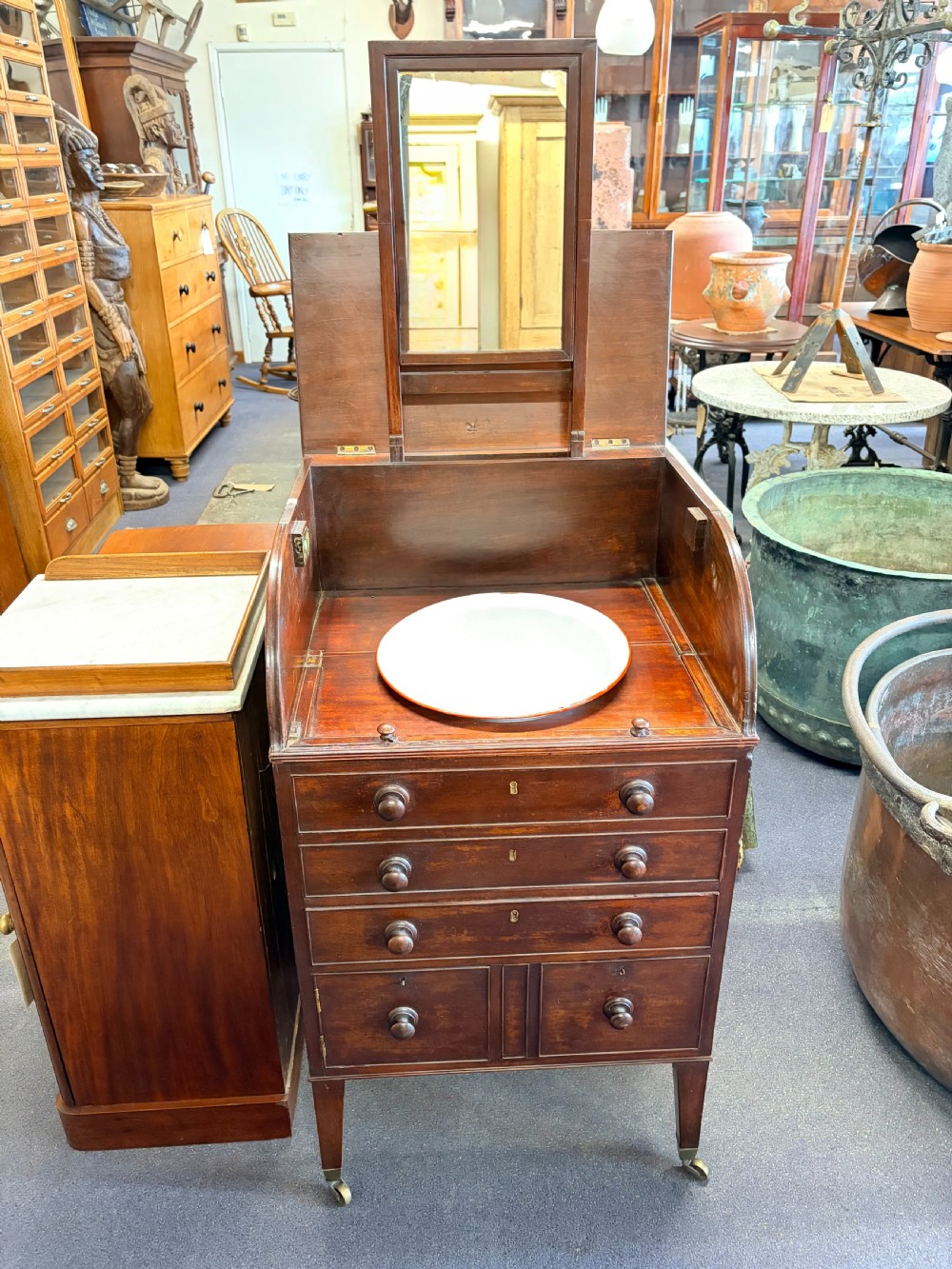 A Georgian mahogany campaign washstand with an open hinged top displaying a rectangular mirror and recessed white basin, above a chest of drawers on tapered legs with brass castors.
