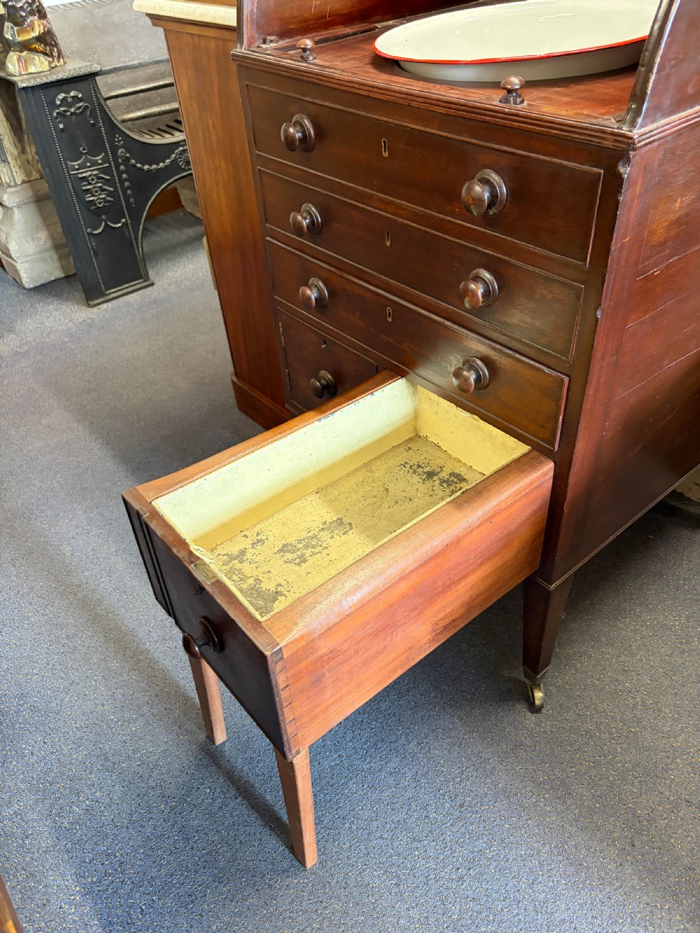 A Georgian mahogany campaign washstand with an open hinged top displaying a rectangular mirror and recessed white basin, above a chest of drawers on tapered legs with brass castors. View XV