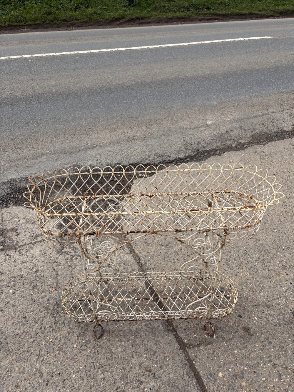 A two-tiered Regency era off-white painted wrought iron wirework plant stand with looped lattice borders and scrolling decorative supports. View II