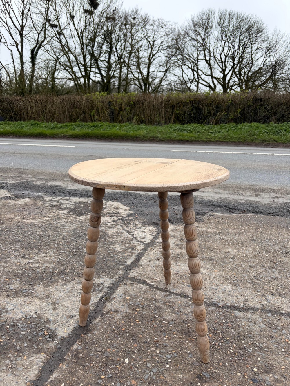 A nineteenth-century pine cricket table featuring a circular top supported by three bobbin-turned legs.