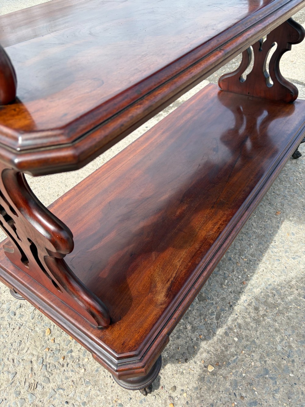 A Victorian mahogany three-tier buffet featuring carved pierced side supports, open rectangular shelves, and turned feet resting on original castors. View III