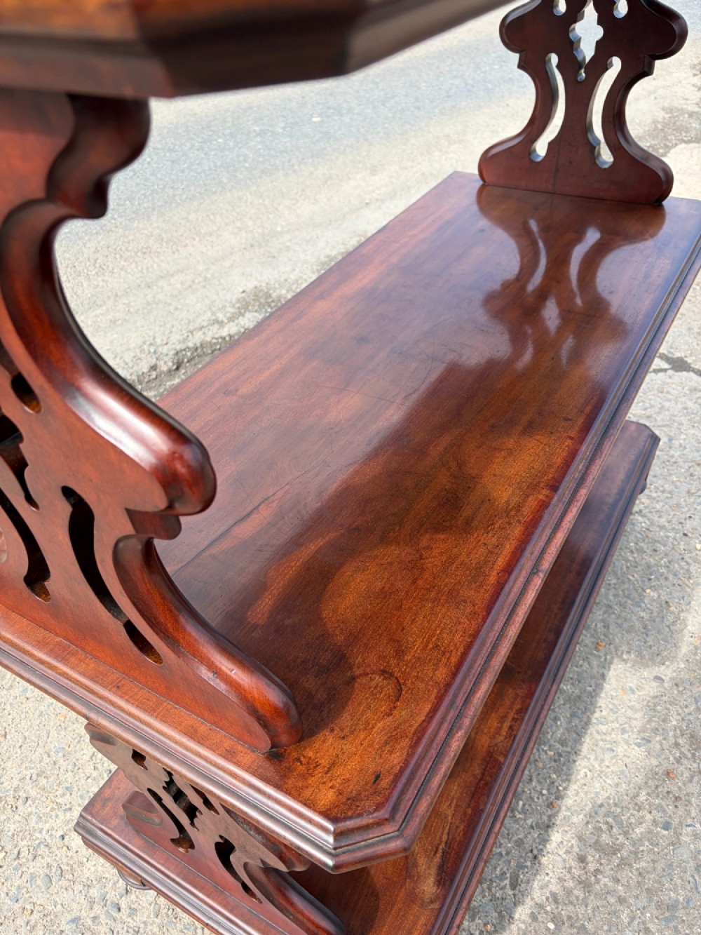 A Victorian mahogany three-tier buffet featuring carved pierced side supports, open rectangular shelves, and turned feet resting on original castors. View IV