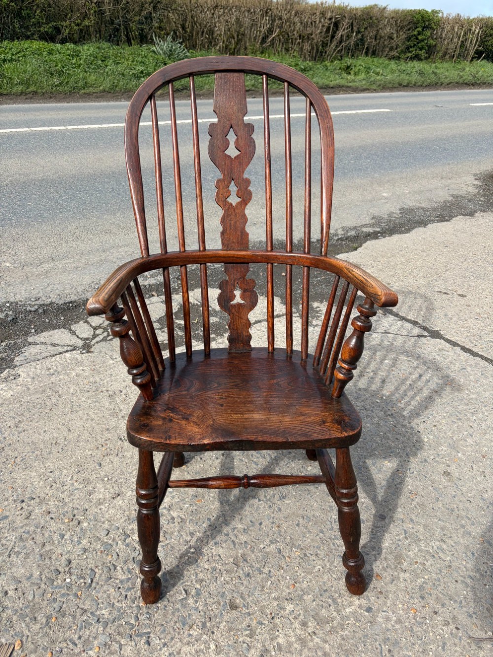 A 19th-century dark elm and beech Windsor armchair featuring a pierced central splat, hoop back, turned spindles, and turned legs.