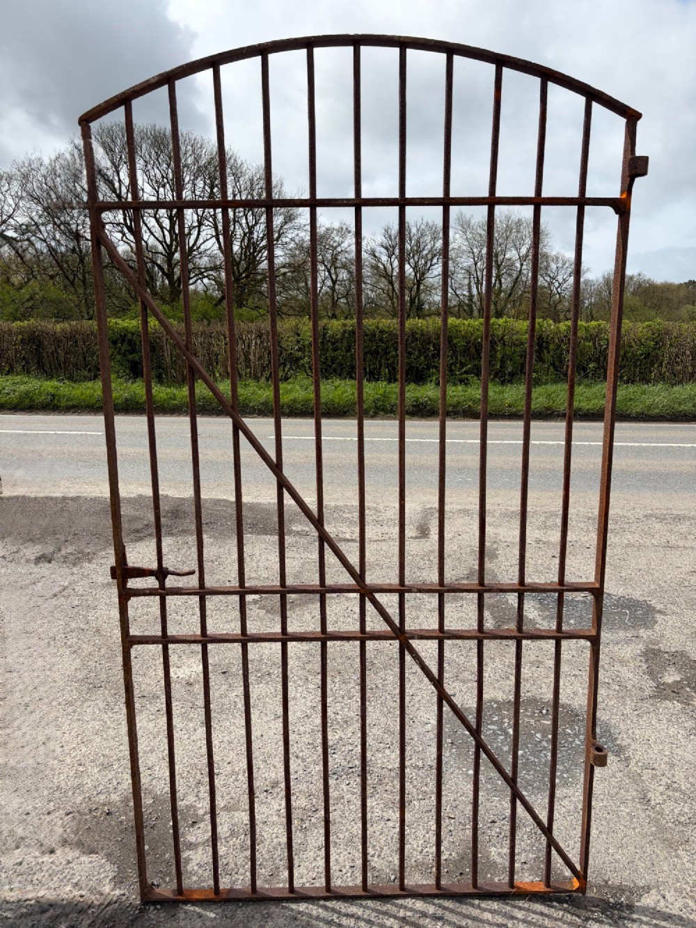A tall late 19th-century wrought iron gate featuring an arched top rail, vertical bars, riveted joinery, and a rusted surface patina.