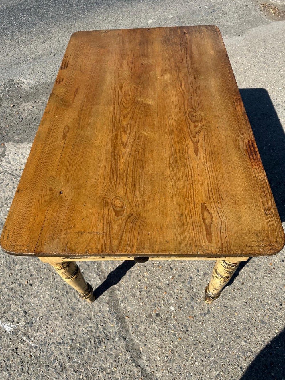 A Victorian pine table featuring a natural wood top, a single drawer with a round wooden knob, and turned yellow painted legs showing light surface wear. View VI
