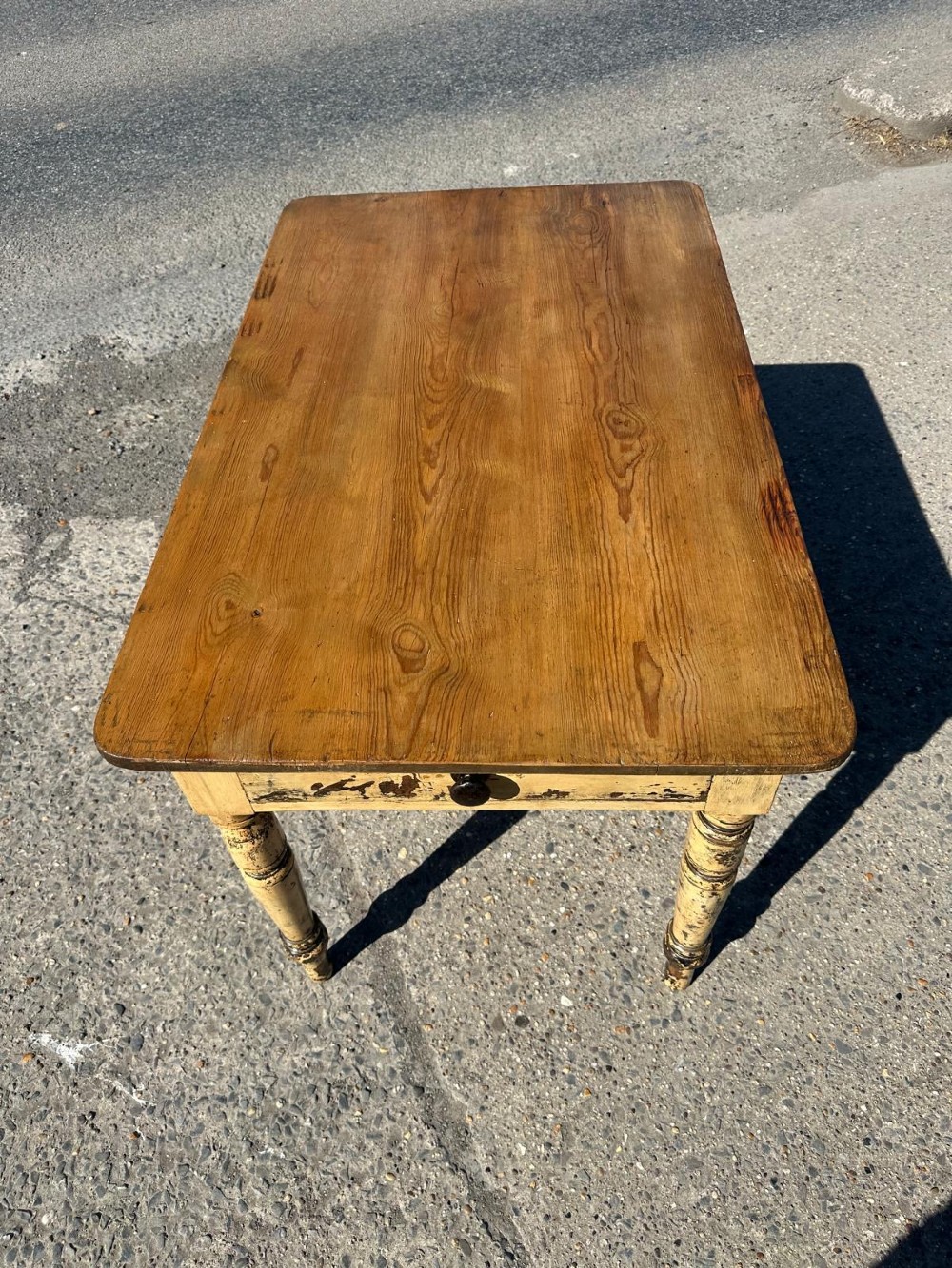 A Victorian pine table featuring a natural wood top, a single drawer with a round wooden knob, and turned yellow painted legs showing light surface wear. View X