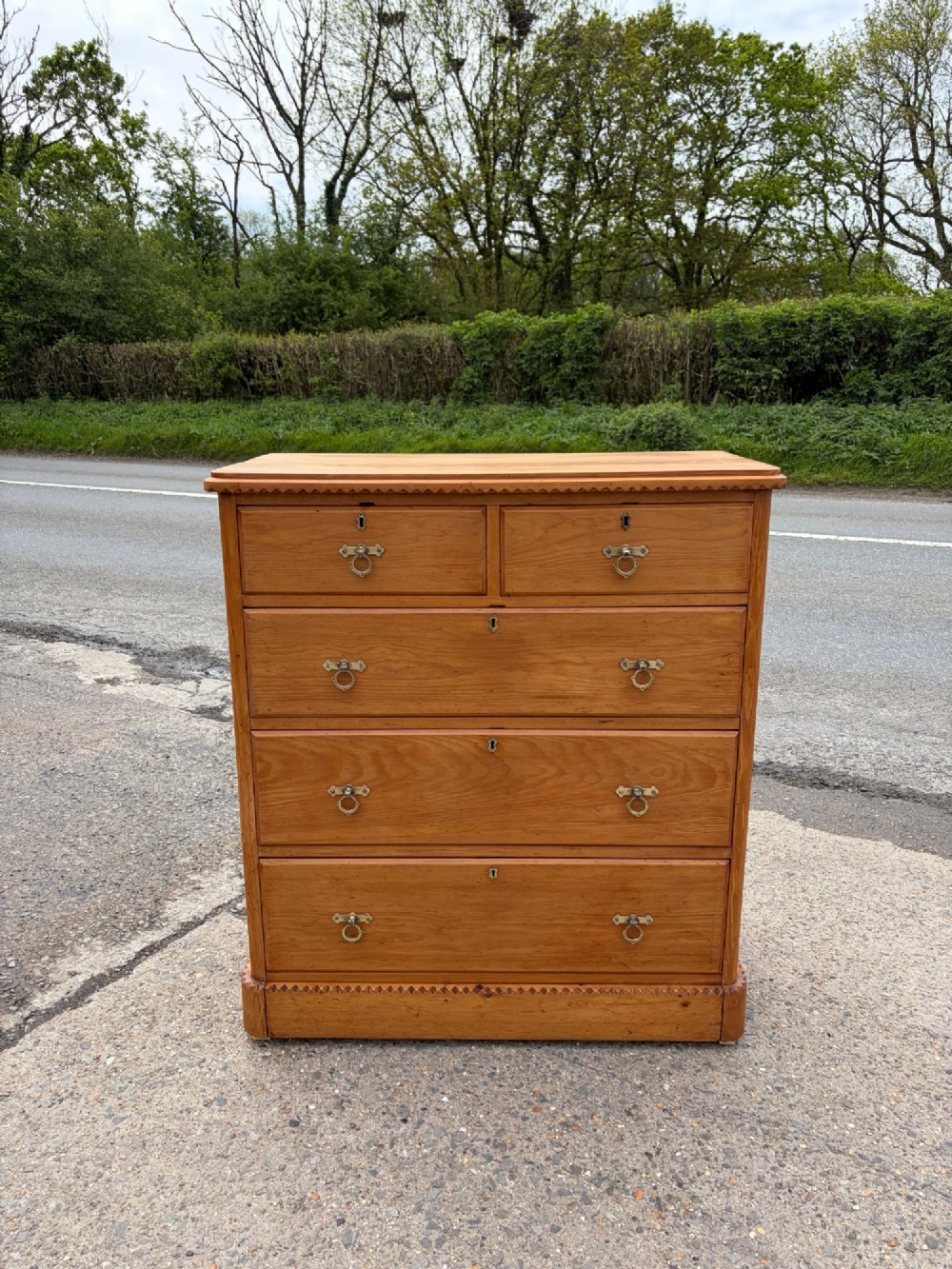 A Victorian pine chest of drawers featuring two short over three long graduated drawers with brass handles and carved edge trim.