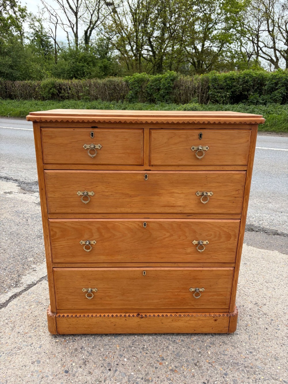 A Victorian pine chest of drawers featuring two short over three long graduated drawers with brass handles and carved edge trim. View II