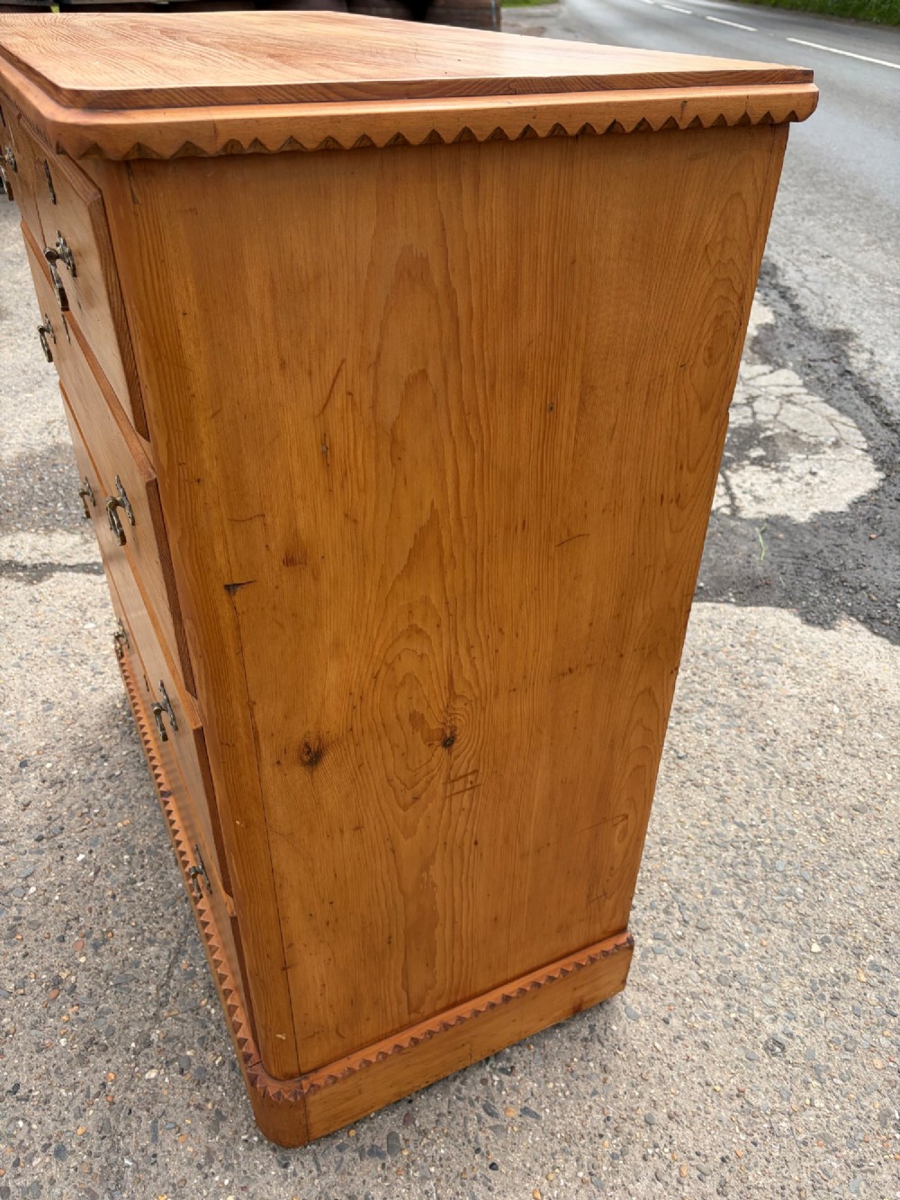 A Victorian pine chest of drawers featuring two short over three long graduated drawers with brass handles and carved edge trim. View VI