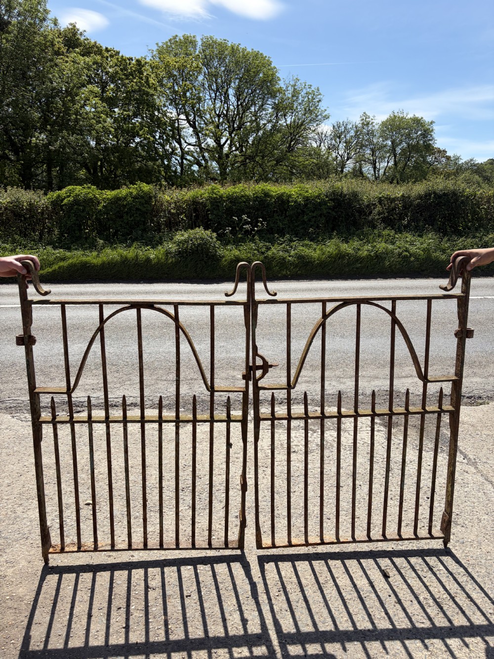 A pair of Victorian wrought iron garden gates featuring vertical bars, arched internal rails, and scroll top embellishments with a natural rusted finish.