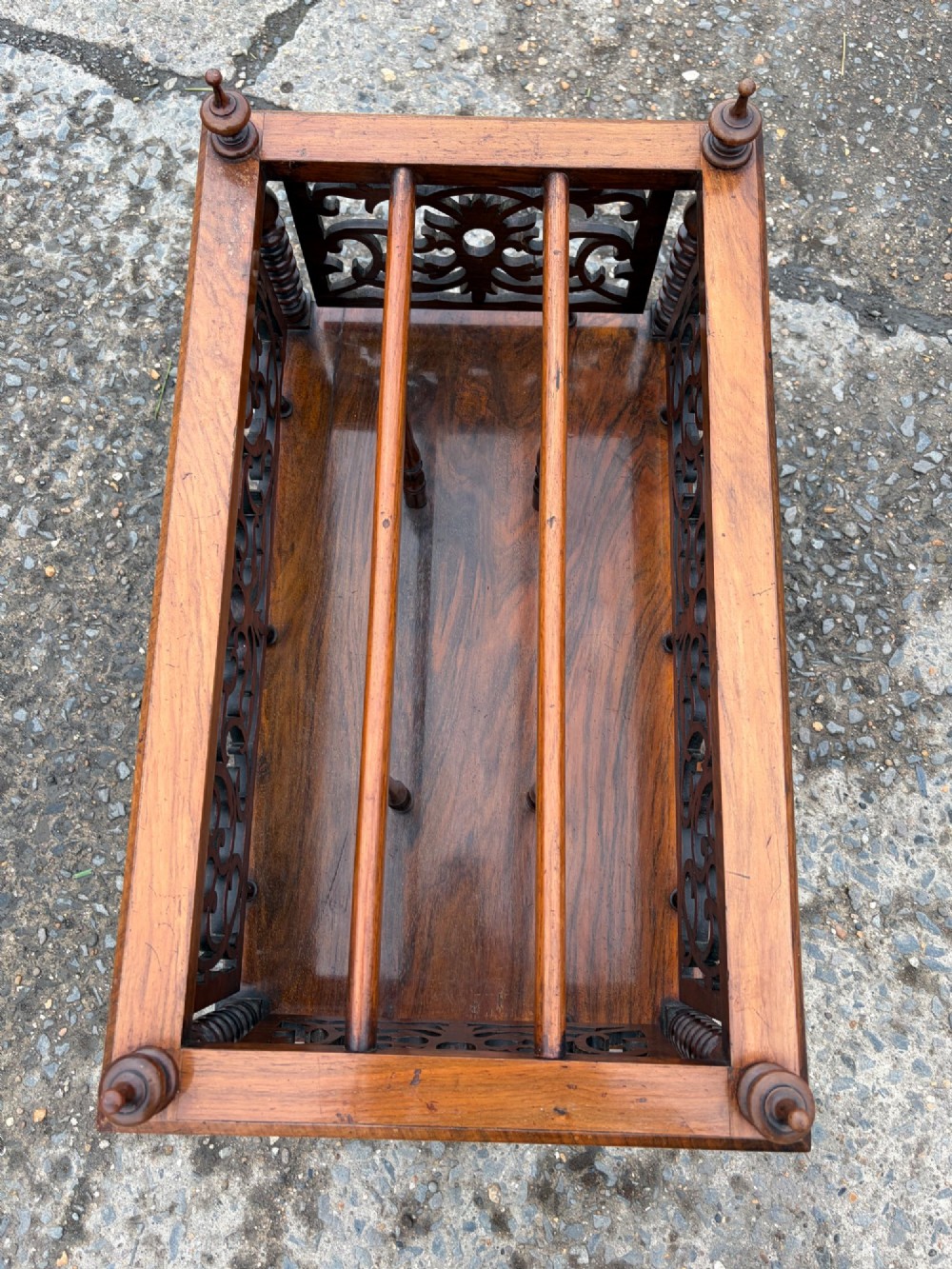 A Victorian walnut canterbury with pierced fretwork dividers, turned corner posts, finials, a lower drawer, and brass castors. View III