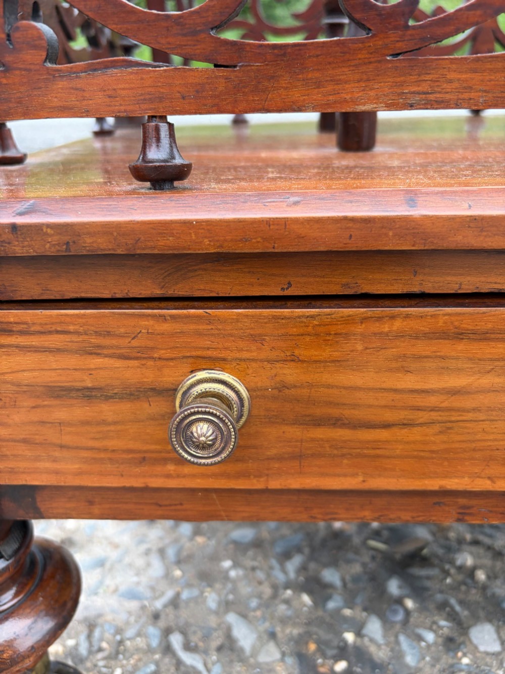A Victorian walnut canterbury with pierced fretwork dividers, turned corner posts, finials, a lower drawer, and brass castors. View V