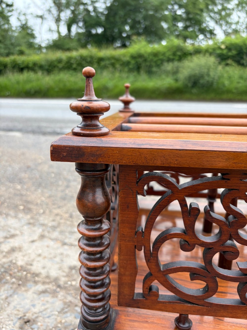 A Victorian walnut canterbury with pierced fretwork dividers, turned corner posts, finials, a lower drawer, and brass castors. View VI