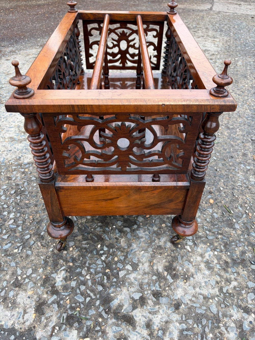 A Victorian walnut canterbury with pierced fretwork dividers, turned corner posts, finials, a lower drawer, and brass castors. View IX