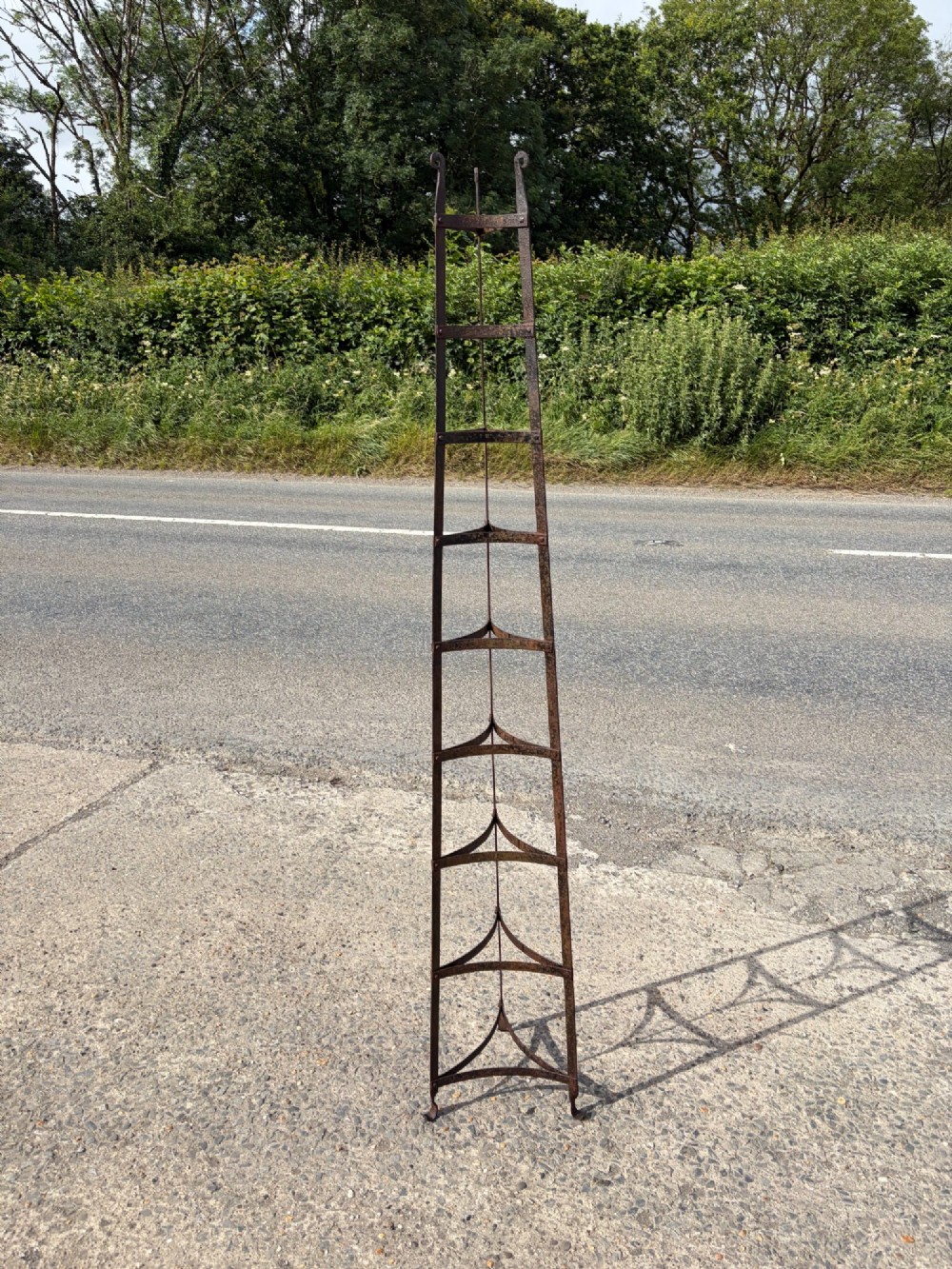 A tall nine-tiered wrought iron pan stand featuring graduated triangular tiers and scrolled detailing at the top.