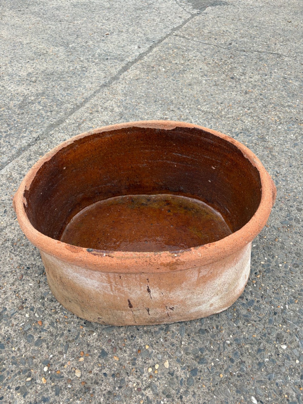 A large 19th-century oval terracotta salting trough with a weathered unglazed exterior and an amber lead-glazed interior.