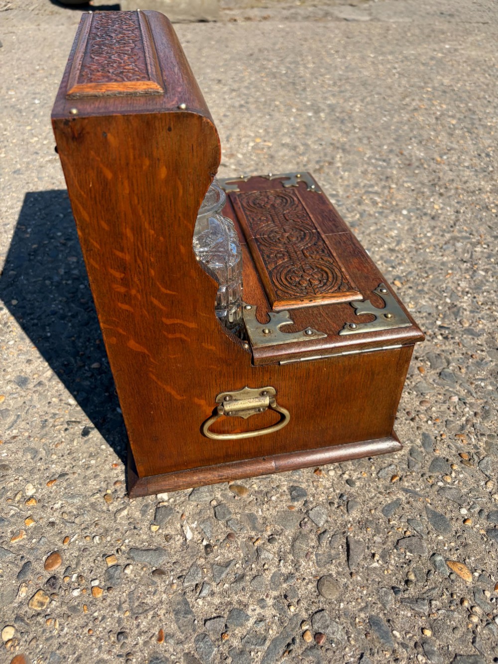 A late Victorian carved oak tantalus set featuring brass corner mounts, a front compartment with carved scrollwork, and three cut glass decanters backed by a mirror. View III