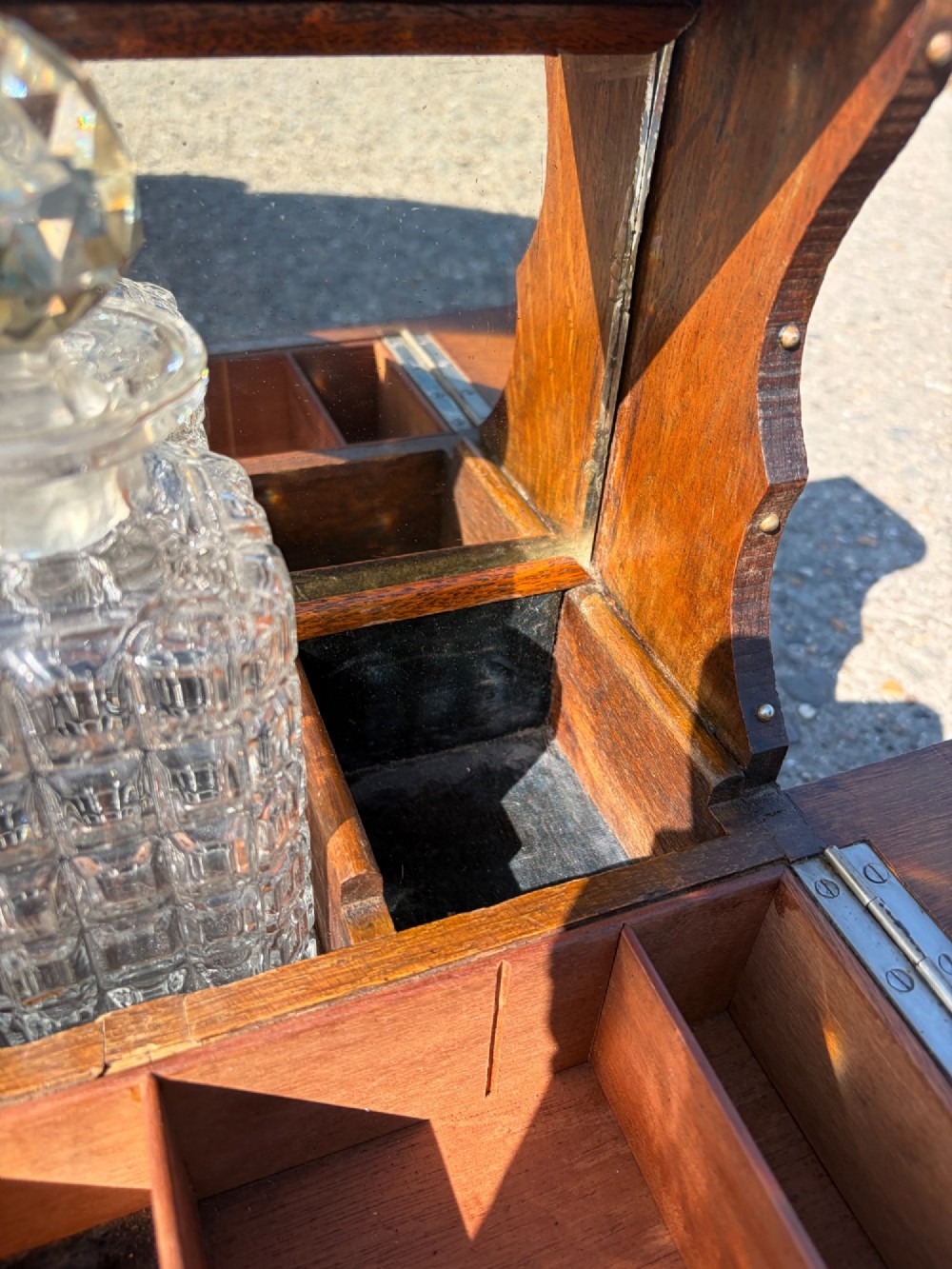 A late Victorian carved oak tantalus set featuring brass corner mounts, a front compartment with carved scrollwork, and three cut glass decanters backed by a mirror. View VI