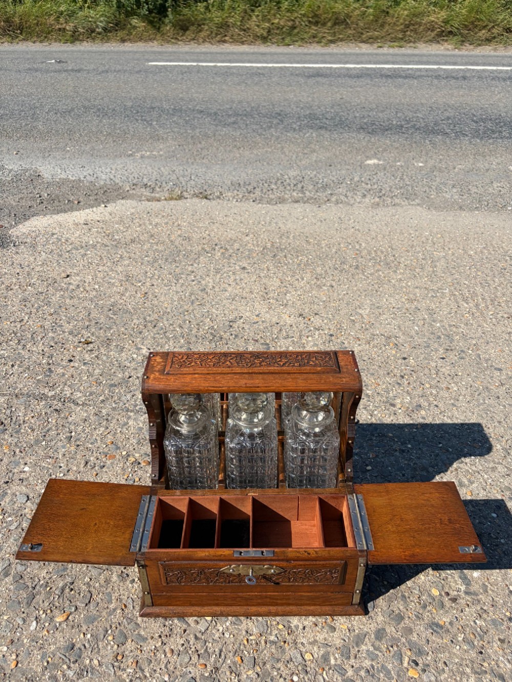 A late Victorian carved oak tantalus set featuring brass corner mounts, a front compartment with carved scrollwork, and three cut glass decanters backed by a mirror. View VII