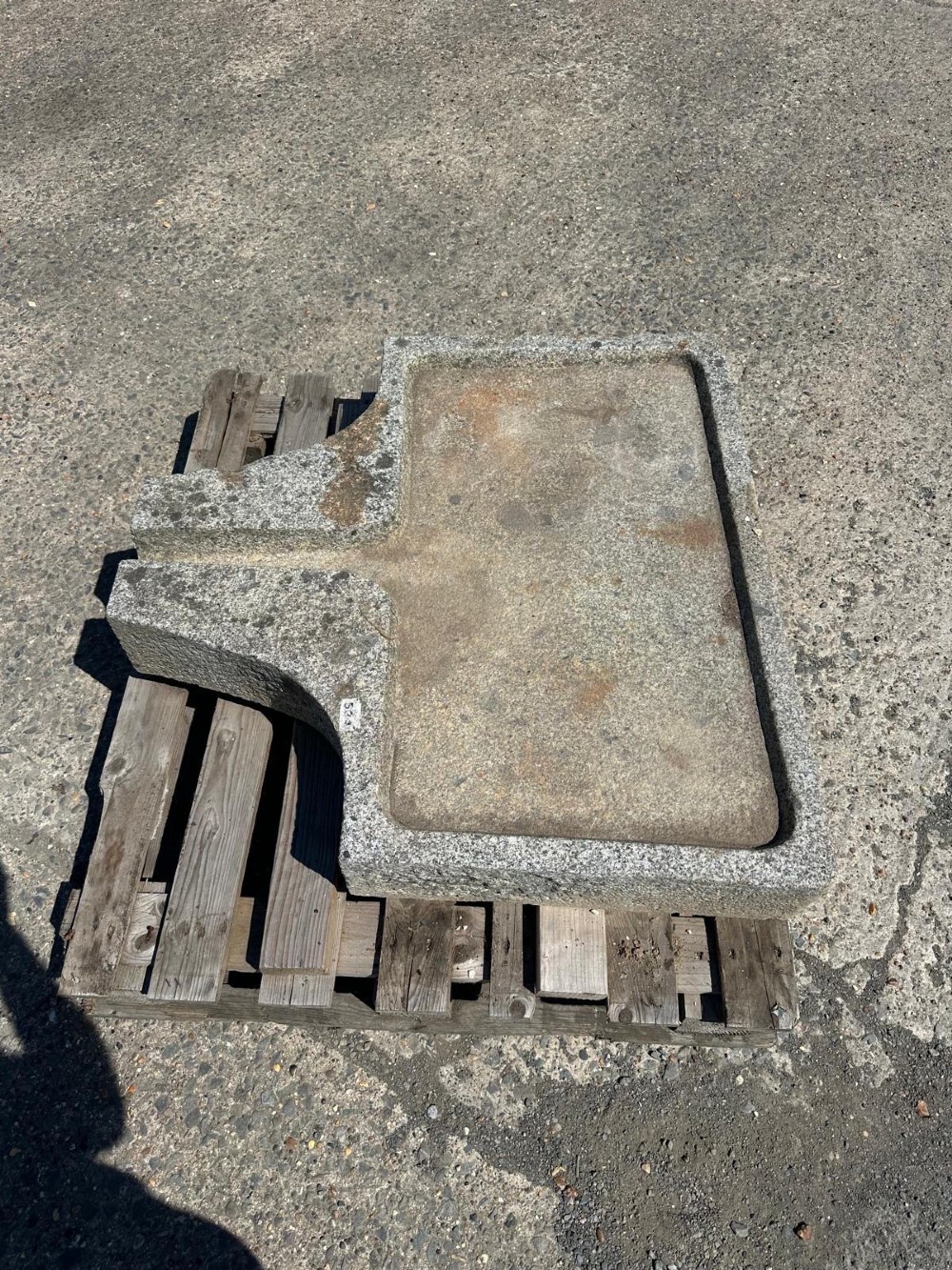 A hand-carved grey granite press stone featuring a recessed rectangular basin with an extended drainage spout.